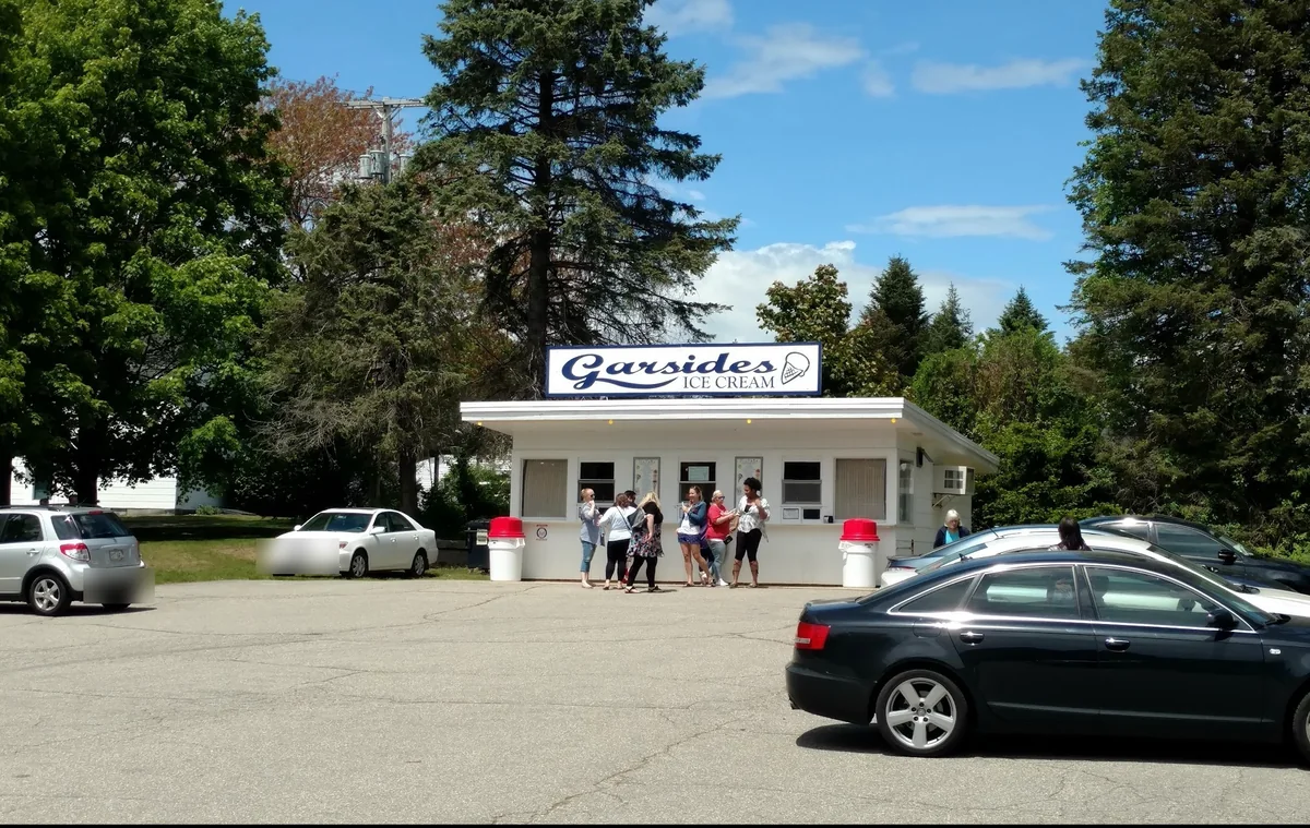 Garside's Ice Cream in Saco, Maine: a small white stand with a blue script sign and a line of customers at the serving windows on a sunny day.
